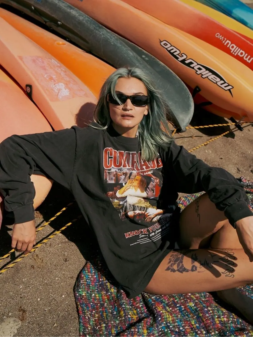 サーフボードの前で黒いグラフィックTシャツを着たモデル